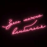 3D model of a pink neon wall sign with Russian script text reading "Здесь можно влюбиться" (Here you can fall in love), emitting a soft romantic glow on a dark background.